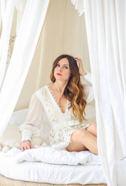 Göz kamaştırıcı bir esmerin portresi, beyaz elbiseli güzel bir genç kız, tente yatağında oturuyor. Güzellik ve moda konsepti