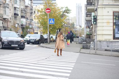 Bej ceketli ve kırmızı çantalı bir kız yaya geçidinden karşıya geçiyor. Avrupa. Sonbahar Moda Konsepti