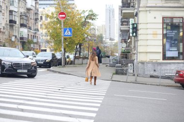 Bej ceketli ve kırmızı çantalı bir kız yaya geçidinden karşıya geçiyor. Avrupa. Sonbahar Moda Konsepti