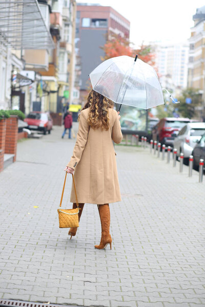 A girl in a beige coat with a transparent umbrella walking down the street. Europe. Travels. autumn Coldly. Weather forecast.