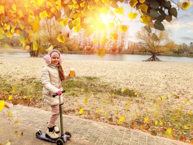 Güzel ve mutlu bir kız sonbaharda plajın yakınında bir scooterla yürüyor. Tatillerde. Uzayı sola kopyala
