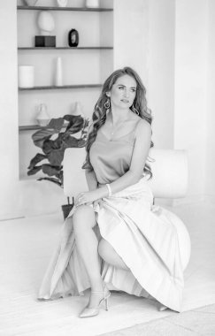 Sandalyede oturan güzel bir kızın çarpıcı siyah beyaz fotoğrafı. Kendine güvenen bir kadın. Moda ve güzellik konsepti