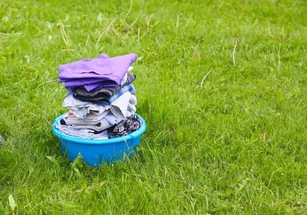 Colorful washed dry clothes in plastic bowl on the green grass background.