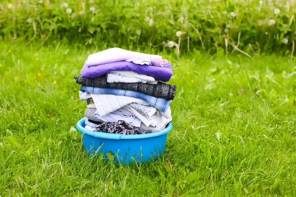 在绿草背景上的塑料碗里 用彩色水洗干衣服 — 图库照片
