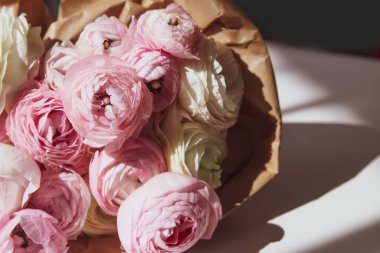 Bir buket Ranunculus güzel narin çiçekler. Çiçek dekoru. Parlak güneş ışığı ve beyaz bir yüzeyde gölgeler.