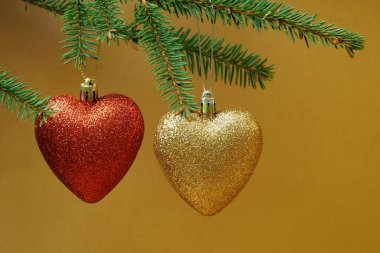 Kalp şeklinde Noel oyuncakları kahverengi arka plandaki bir Noel ağacının yeşil dalına asılır. Yan görünüş. kopyalama alanı. Noel zamanı. Yüksek kalite fotoğraf