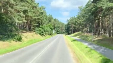 Bereketli yapraklarla çevrelenmiş sessiz bir kır yolu, mavi gökyüzünün altında, ara sıra bulutlarla. Bu çekici manzara açık hava yaşam tarzı tanıtım materyalleri, seyahat broşürleri veya çevre için idealdir.