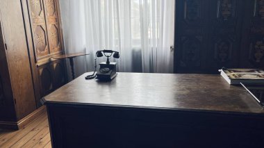 Çizik ahşap bir masada eski bir telefon, sıcak ışık, bulanık arka plan, klasik tasarım, nostaljik atmosfer.