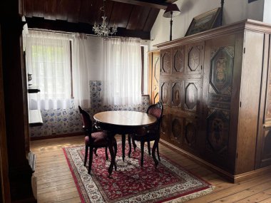 Mosty, Polonya - 28 Haziran 2025: Yuvarlak ahşap bir masa ve zarif döşemeli koltukları olan büyüleyici bir yemek odası, narin bir avizeyle aydınlatılmış. Alan, dik perdeli büyük pencerelere sahiptir.