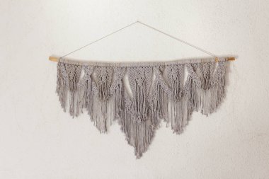 Beyaz bir duvarda asılı gri makrome süsleme. Boho el yapımı dekorasyon