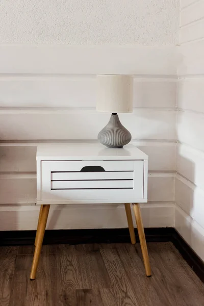 White wooden bedside table with lamp near white wooden wall