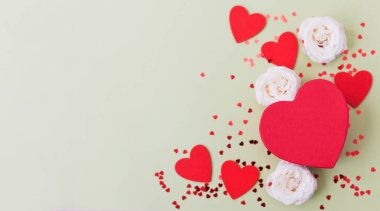 Valentines day theme background banner with red heart shaped box, white roses and red hearts confetti on a green background, copy space