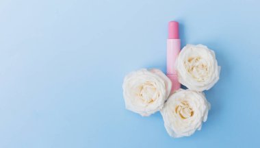 Pink lipstick and white roses on a blue background, copy space. Beauty concept banner