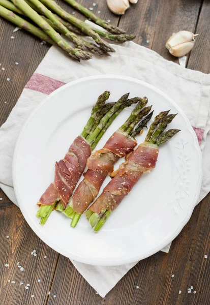 Asparagus with ham on a white plate with garlic and salt. Tasty spring dish with asparagus and bacon