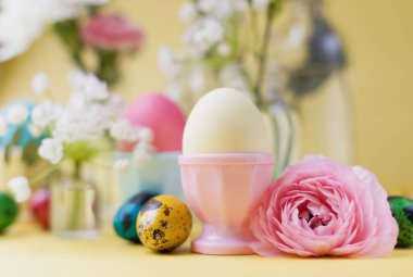 Sarı arka planda Paskalya yumurtaları ve çiçekler. Paskalya arkaplanı ve pastel renkler. Bahar tatili kavramı