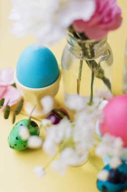 Sarı arka planda Paskalya yumurtaları ve çiçekler. Paskalya arkaplanı ve pastel renkler. Bahar tatili kavramı