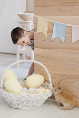 Paskalya süslemeleriyle donatılmış hafif bir mutfakta sevimli bir tavşanı olan beyaz bir çocuk.