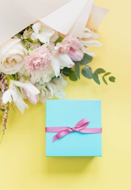 Beautiful bouquet with roses, carnations, iris and eucalyptus and blue gift box with pink ribbon on a yellow background, copy space. Mothers day, 8 march, holiday gift concept