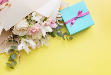 Beautiful bouquet with roses, carnations, iris and eucalyptus and blue gift box with pink ribbon on a yellow background, copy space. Mothers day, 8 march, holiday gift concept