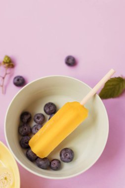 Bright colorful popsicles in colorful bowls with berries and ice cubes on a light violet background. Tasty ice pops close up