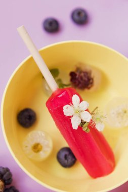 Bright colorful popsicles in colorful bowls with berries and ice cubes on a light violet background. Tasty ice pops close up