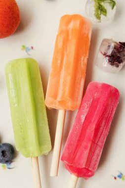 Bright colorful popsicles on a white tray with berries and ice cubes on a light violet background. Tasty ice pops close up