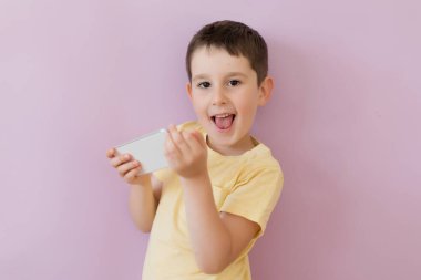 Caucasian boy in yellow t-shirt holding smartphone on a pink background with copy space