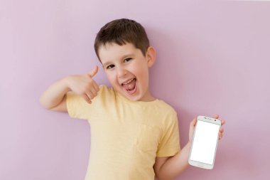 Caucasian boy in yellow t-shirt holding smartphone and showing white blank screen for text space on a pink background with copy space