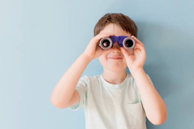 Caucasian boy with toy binoculars on a blue background with copy space. Travel funny concept