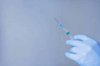 Mavi bir arka planda şırınga tutan mavi eldivenler ve fotokopi alanı.