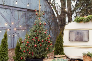 Vintage old travel trailer with Christmas decorations, Christmas tree, chair and Christmas lights. Cozy home, camping before Christmas holidays. clipart