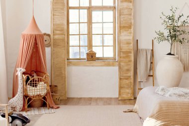 Light playroom interior with rattan crib with canopy, wicker baskets, toys and big window