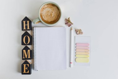 Flat lay with empty open notebook, cup with coffee, sticky post it and black wooden home decoration on a white background, copy space