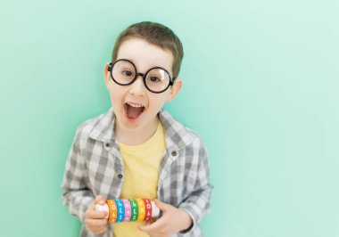 Gözlüklü, açık yeşil arka planda matematik öğrenme oyuncağı olan, gözlüklü, beyaz anaokulu çocuğu.