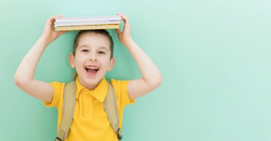 Okul çantalı beyaz okul çocuğu, açık yeşil arka planda, üzerinde fotokopi alanı olan bir kafanın üzerine kitap yapıştırıyor.