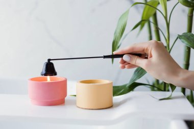 Craft pink and orange soy candles on baththube near bamboo plant at white light bathroom interior. Woman extinguish candle with black candle snuffer clipart