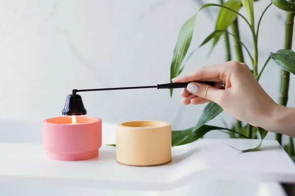 Banyonun iç tarafındaki bambu bitkisinin yanında küvette pembe ve turuncu soya mumları. Kadın mumu siyah mum söndürücüyle söndürür.