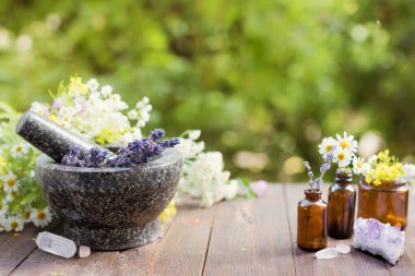 Homeopati ve bitkisel tıp konsepti. Çiçek ve bitkilerle granit havan ve tokmak, çiçekli cam şişeler ve doğa kristalleri taşlar