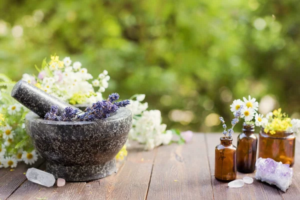 Homeopati ve bitkisel tıp konsepti. Çiçek ve bitkilerle granit havan ve tokmak, çiçekli cam şişeler ve doğa kristalleri taşlar