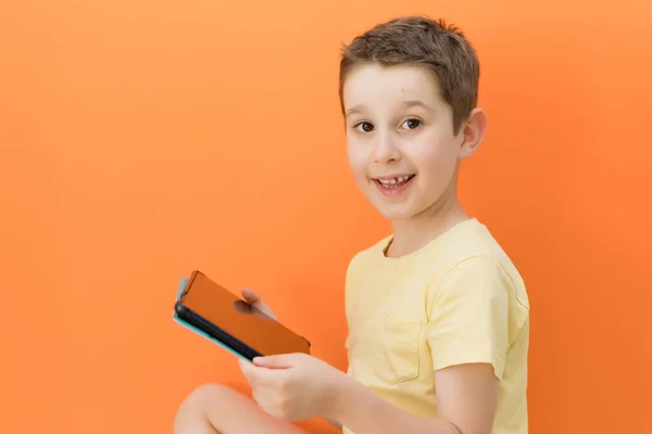 Blanke Jongen Met Tablet Een Oranje Achtergrond Met Kopieerruimte — Stockfoto