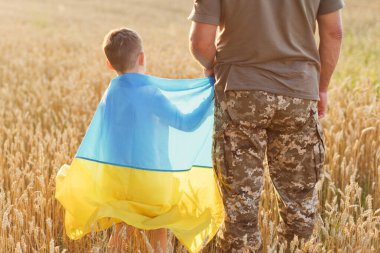 Buğday tarlasında Ukrayna bayrağı taşıyan asker ve çocuk. Ukrayna 'nın bağımsızlık günü kavramı. Ukrayna 'daki savaşı durdurun. Ukrayna 'yı Kaydet