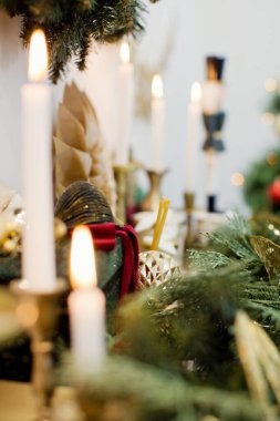 Green and red Christmas decoration and burning candle on a fireplace