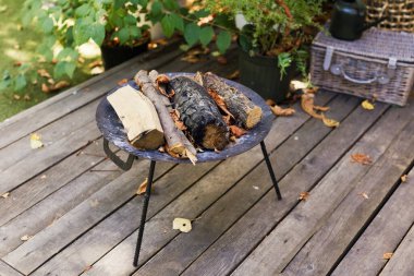 Arka bahçedeki ahşap terasta metal şöminede kuru odun kütükleri.