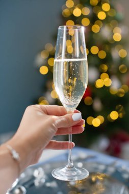 Woman holds glass of champagne on a Christmas tree lights background. New year eve concept
