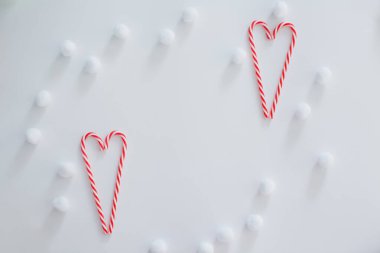 Heart shaped candy canes and white fluffy decorative snowballs on a white background with copy space. Christmas frame concept