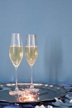 Vintage silver tray with glass of champagne, christmas bells, burning sparklers and silver confetti on a blue background with copy space