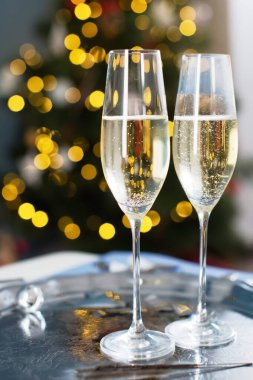 Noel ağacı arka planında şampanya kadehleri, Noel çanları, maytaplar ve gümüş konfetileri olan klasik gümüş tepsi.