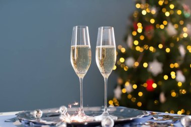 Vintage silver tray with glasses of champagne, christmas bells, burning sparklers and silver confetti on a Christmas tree background with copy space