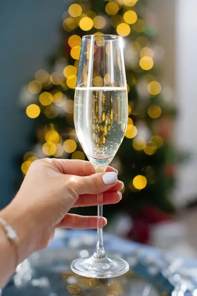 Woman holds glass of champagne on a Christmas tree lights background. New year eve concept