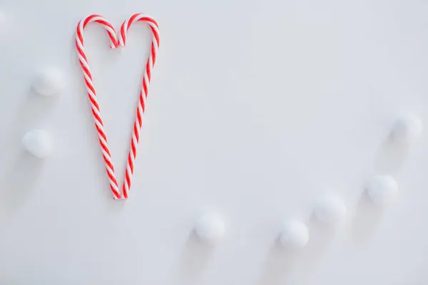 Heart shaped candy canes and white fluffy decorative snowballs on a white background with copy space. Christmas frame concept